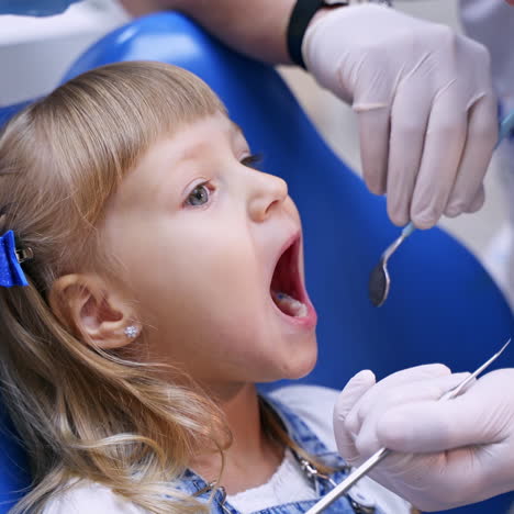 Little girl at the dental office. Male dentist examines child's mouth. Lovely kid sitting in dentist chair. Healthcare concept.