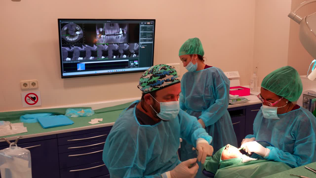 Panning left shot of two dentists operating in the clinic and assistant helping in background with the tools and administrative assets