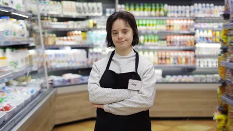 Portrait-of-a-shot-worker-with-Down-syndrome-standing-with-crossed-hands-at-supermarket