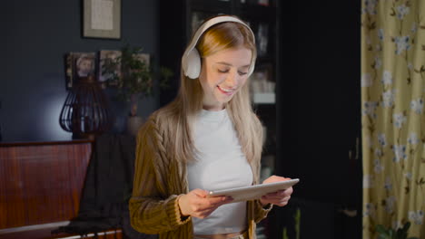 happy young woman with headphones listening music on tablet and dancing in living room at home 1