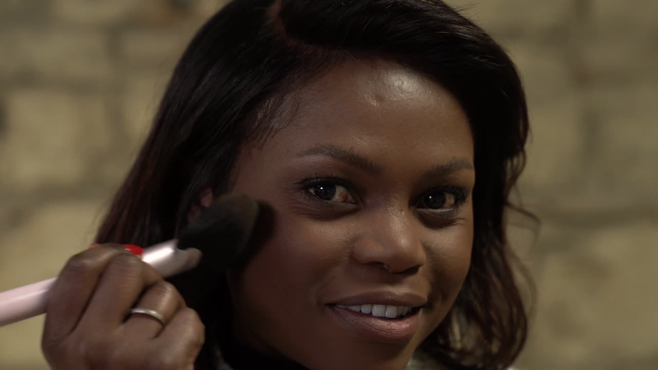 Close up black girl smiling in the camera applying makeup, powdering brush