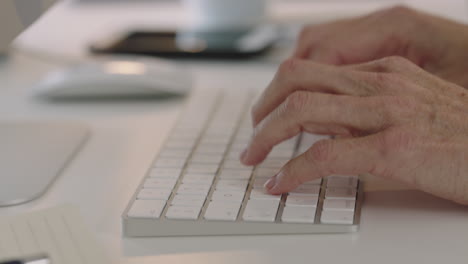 close up mature woman hands typing using computer keyboard technology on office desk