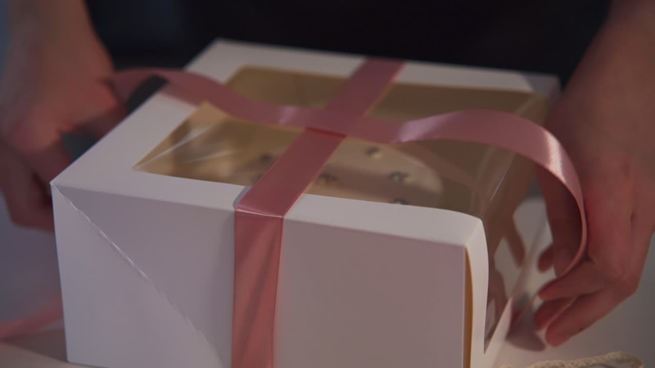 Hands Tying Pink Ribbon Around a White Cake Box