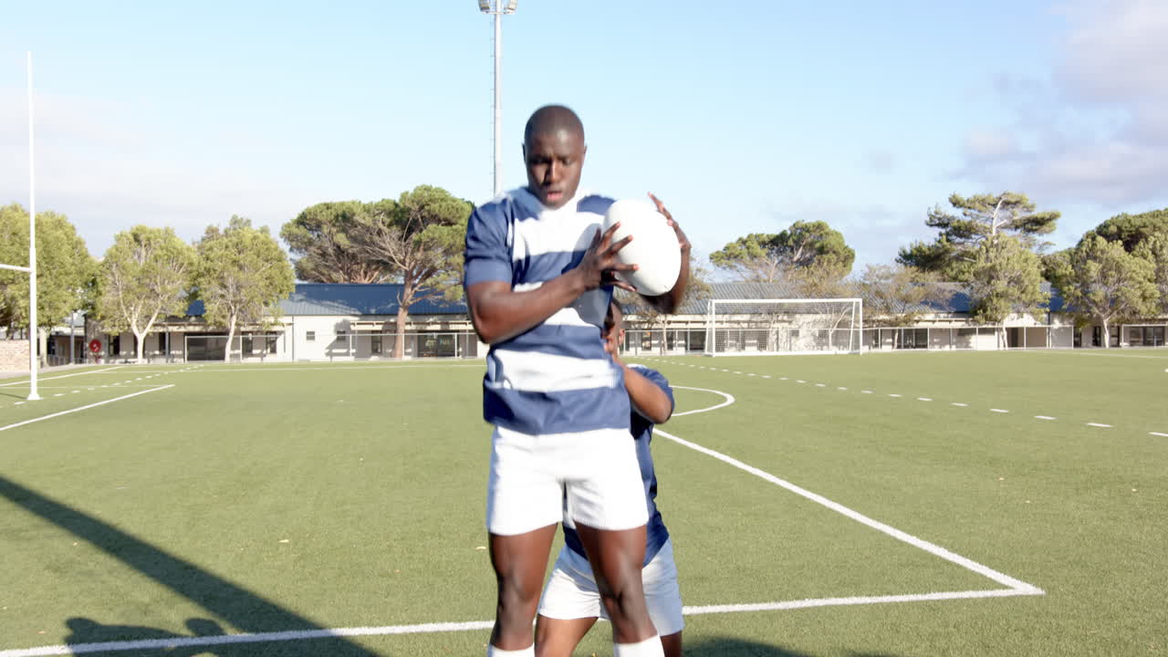 Playing football, two african american men in blue jerseys competing for ball on field