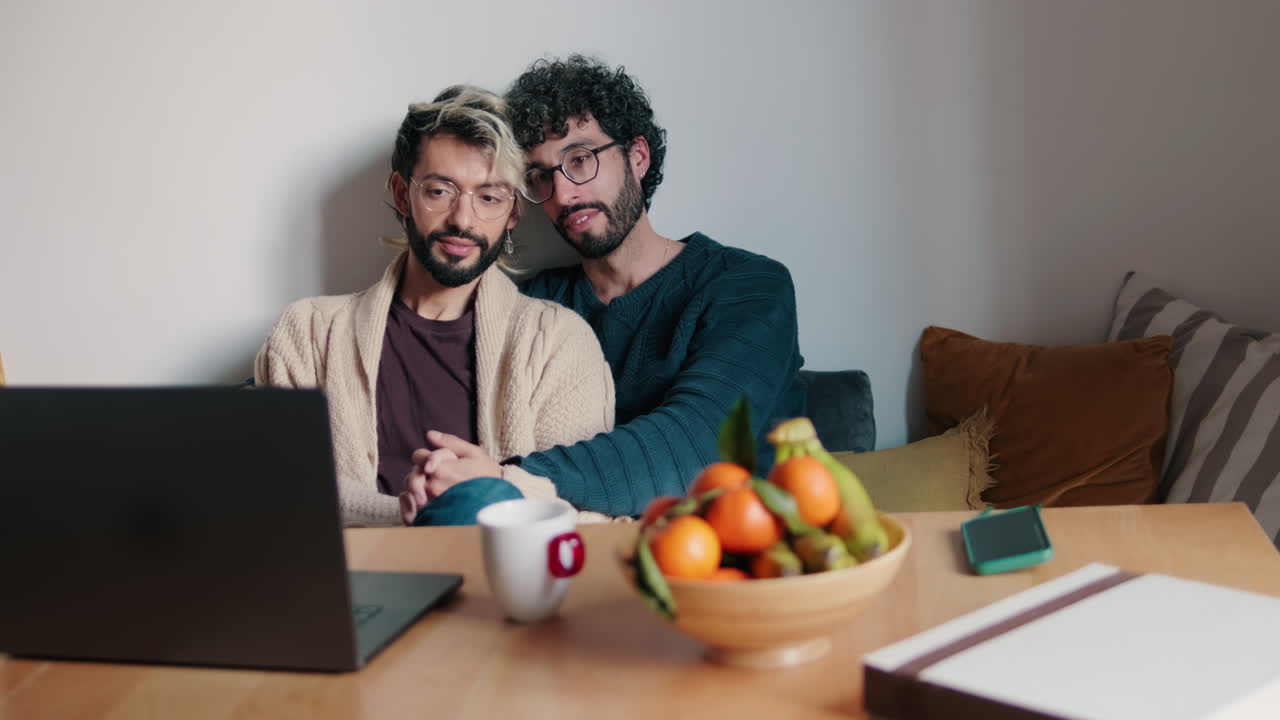 Gay Couple Holding Hands and Using Laptop at Home