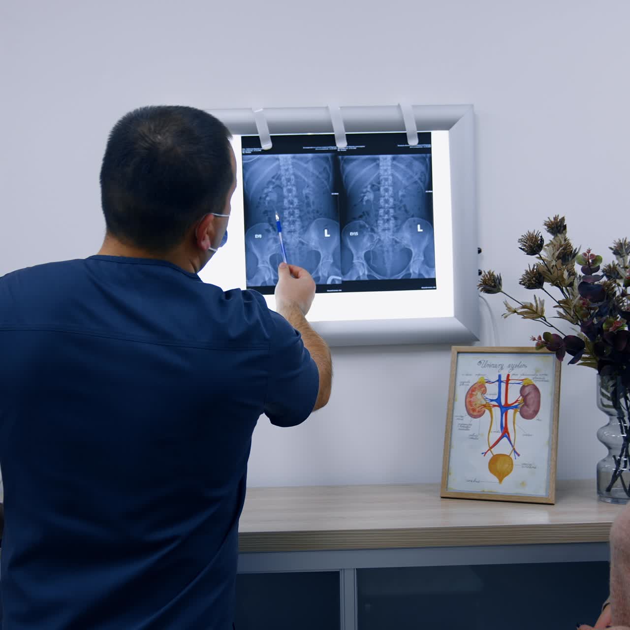 Patient and doctor standing in the hospital cabinet. Medic explaining the x-ray scan hanging on the light screen