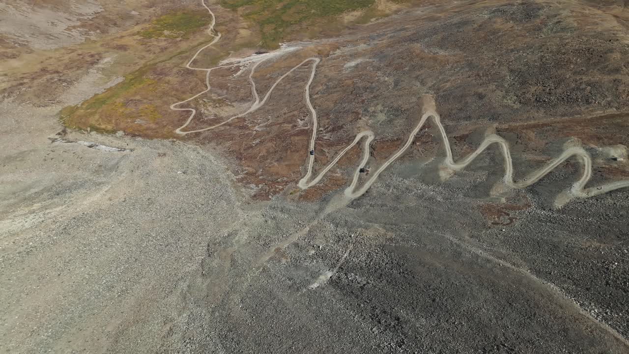 Panoramic aerial overview of offroad car driving up steep dirt switchbacks on gravel mountainside