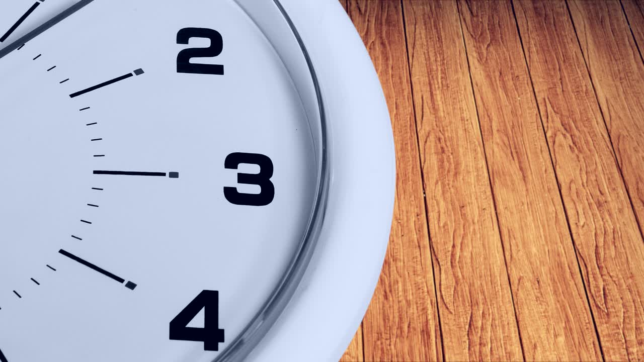 Video footage of a white clock face with a ticking arrow and numbers, shot with wooden background