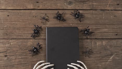 video of halloween skeleton hands, notebook and spiders with copy space on wooden background