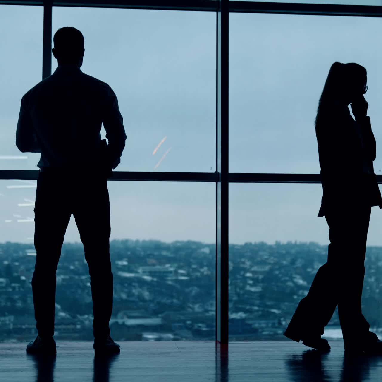 Male silhouette stands his back to camera drinking coffee. Female silhouette walks to and fro speaking on the phone