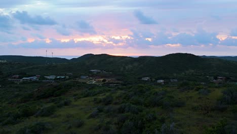 Pastel-yellow-orange-hues-spread-in-clouds-as-drone-rises-above-Caribbean-island-hiking-hills-and-school