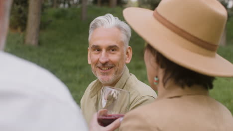 hombre canoso hablando con una mujer que bebe vino tinto durante una fiesta al aire libre en el parque