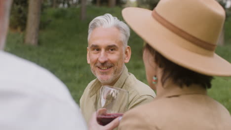 gray haired man talking with a woman who drinking red wine during an outdoor party in the park