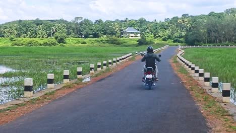 wearing z-marked shoes , a man wears a helmet on a motorbike and passes by on a rural road in india , traveling on an old motorbike