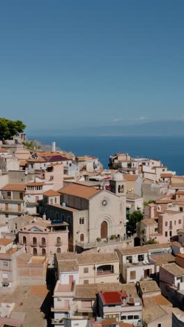 vertical drone shot flying over castelmola town in sicily. historic town up in the mountains on the edge of cliff. aerial view of natural terrace urban settlement.