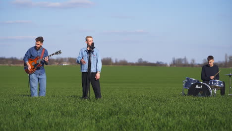 guitarist, drummer and singer make performance among the fields. young men musicians play music in the nature backdrop.