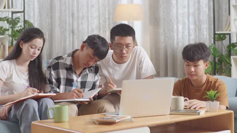 asian teen group studying on a laptop at home, sitting on sofa, taking online course, writing into notebook