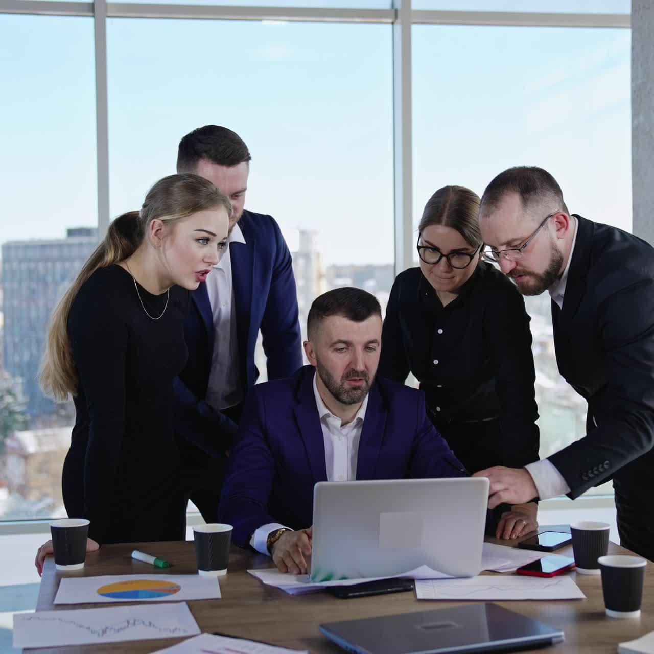 Small business team collaboration. Colleagues gathered around their chief sitting at the desk in front of laptop. Cityscape at the backdrop