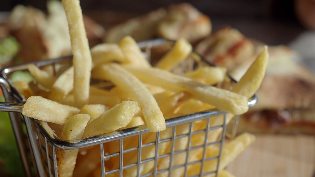 Hand Picking a Crispy Golden French Fry from a Metal Basket