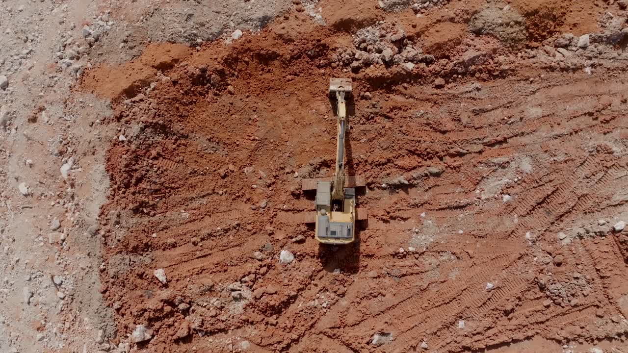 Top down aerial footage of a backhoe that is moving clay around at the edge of a quarry.