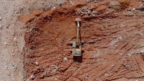 top down aerial footage of a backhoe that is moving clay around at the edge of a quarry.