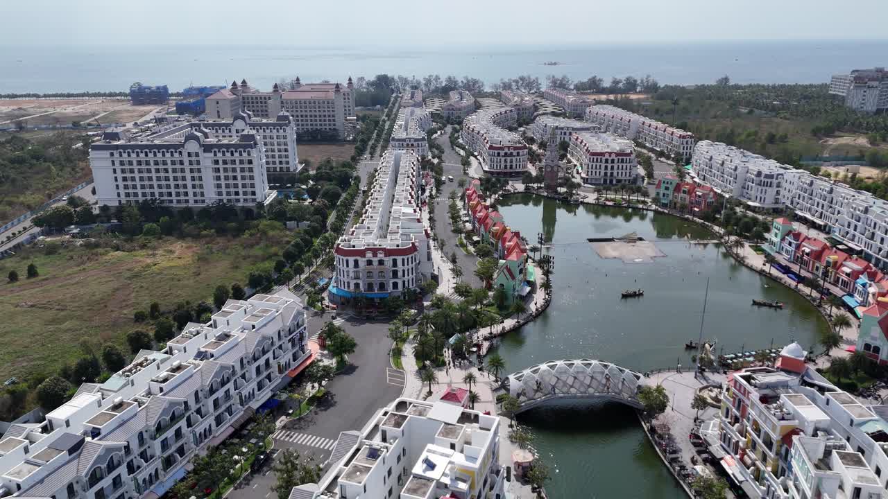 Aerial footage shows architectural style, where rows of colorful buildings stand closely along both banks of a narrow waterway A charming bridge connecting the vibrant districts. Newly built town.