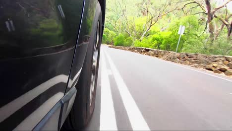 Car-POV-from-road-facing-front-right-wheel-driving-down-bitumen-road-down-a-hill-into-town