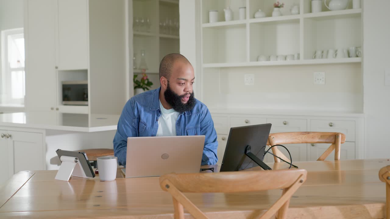 Yawning, African American man stretching then leaning and typing on laptop, working at home table