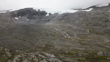 un gran glaciar en una montaña rocosa con algunas pequeñas cascadas y ríos en un entorno brumoso, noruega, europa, dron