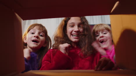 three siblings children girls unpacking delivery parcel at home, inside viev from cardboard gift box