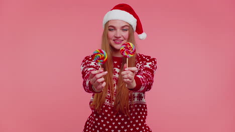 joyful girl in red christmas sweater, hat presenting candy striped lollipops, stretches out hands