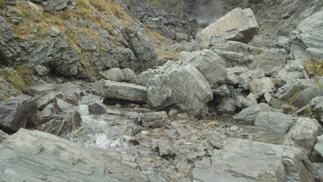 Water-flows-thru-rocks-with-waterfall-in-the-backround