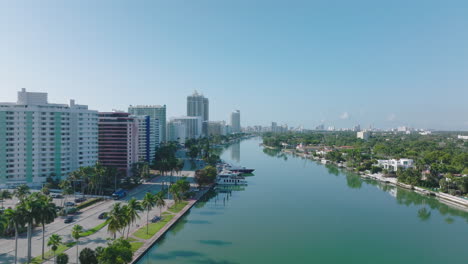 Forwards-fly-above-calm-water-surface-in-city-on-sunny-day.-Row-of-tall-apartment-houses-in-residential-urban-borough.-Miami,-USA