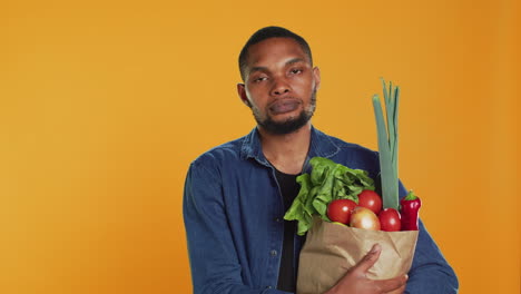 retrato de un hombre afroamericano sosteniendo una bolsa de papel llena de comida biológica