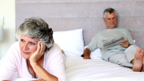 woman thinking while her husband is reading a newspaper