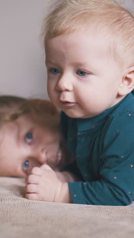 lovely blonde sister hugs cute brother nibbling yellow circle on large comfortable bed in light room at home
