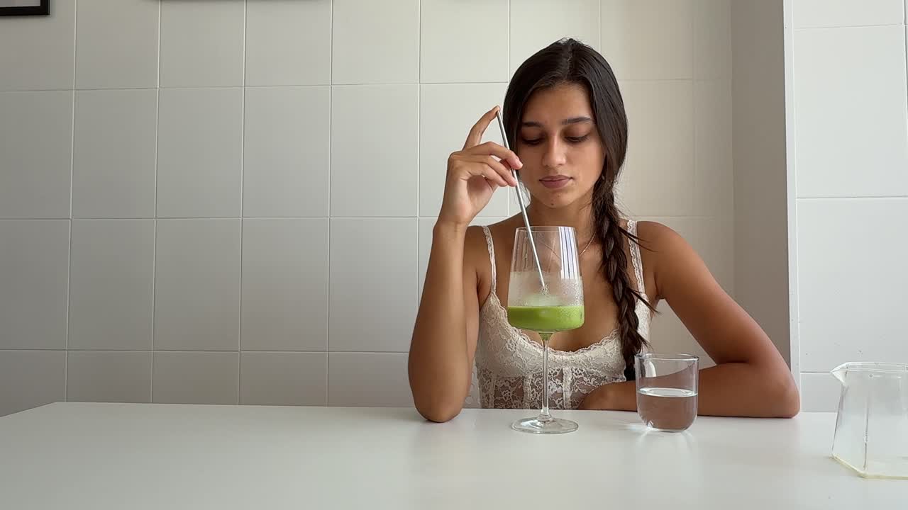 Giovane donna che mescola uno smoothie verde a un tavolo bianco
