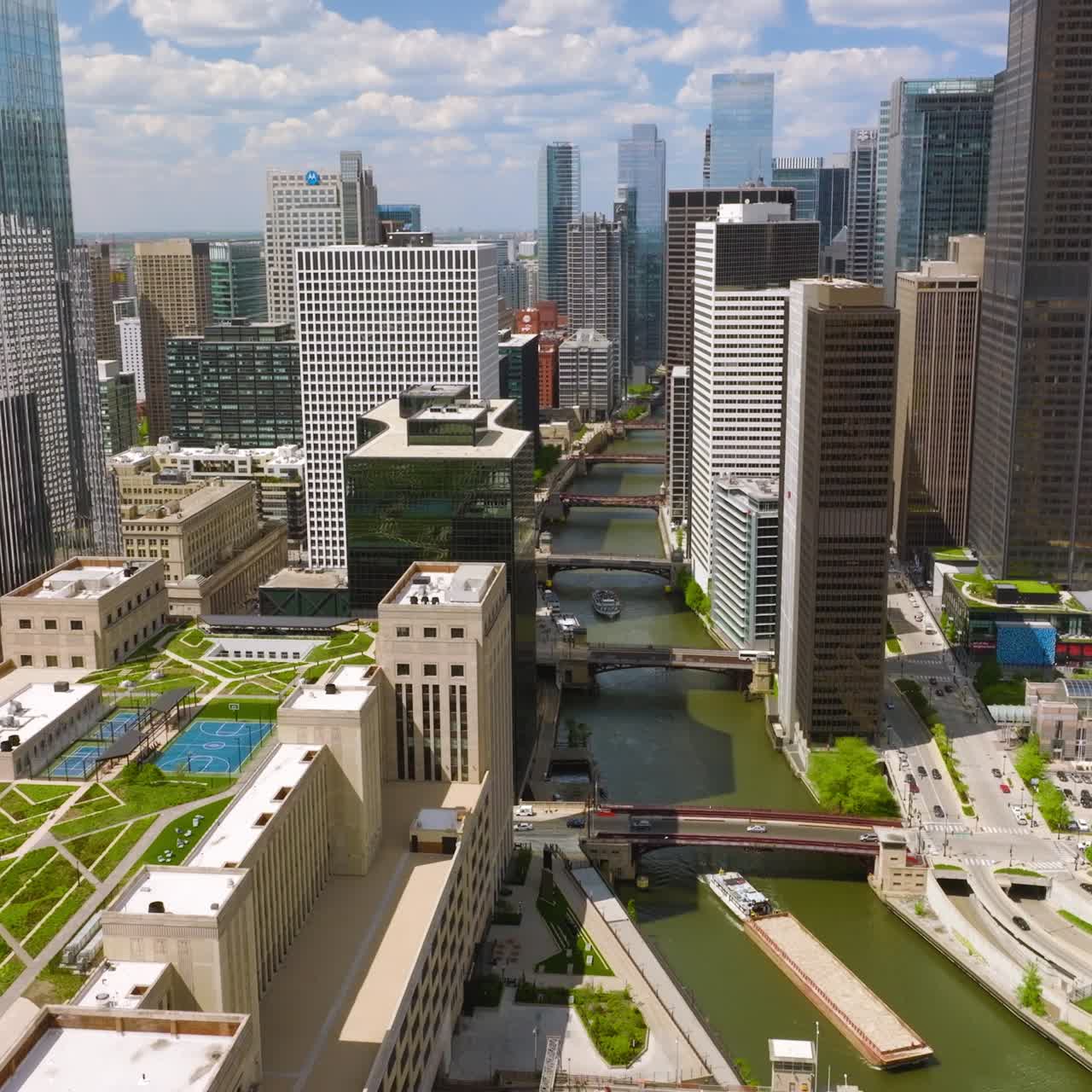 Fantastic buildings of great Chicago. Drone flying over the buildings with green areas on tops, over the river with multiple bridges on. Cloudy sky at backdrop