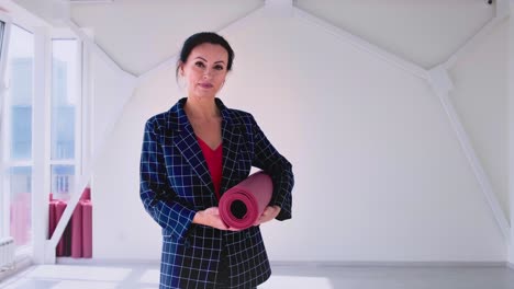 a woman shifts from a thoughtful pose to a confident stance, transitioning with a yoga mat in a bright, spacious studio, emphasizing mindfulness and fitness