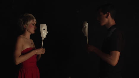 a couple faces each other and covers their faces with white masks