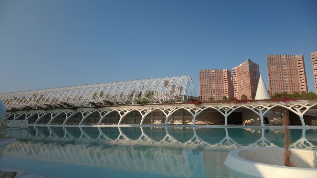 Still reflective pool mirrors white lattice canopy and terracotta high-rise buildings, creating calm upscale city atmosphere, strong symmetry, and spacious contemporary rooftop setting