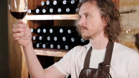 authentic shot of successful male sommelier is tasting a flavor and checking white wine quality poured in transparent glass in a wine cellar.