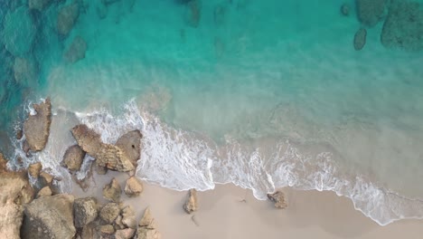 Toma-Aérea-De-Arriba-Hacia-Abajo-De-Rocas-En-La-Playa-De-Arena-Y-Olas-Que-Llegan-Del-Mar-Caribe---Playa-Chencho,-República-Dominicana