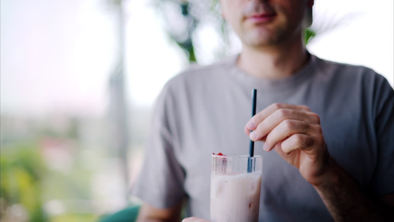 Man mixing and drinking a strawberry drink with a black straw at a restaurant