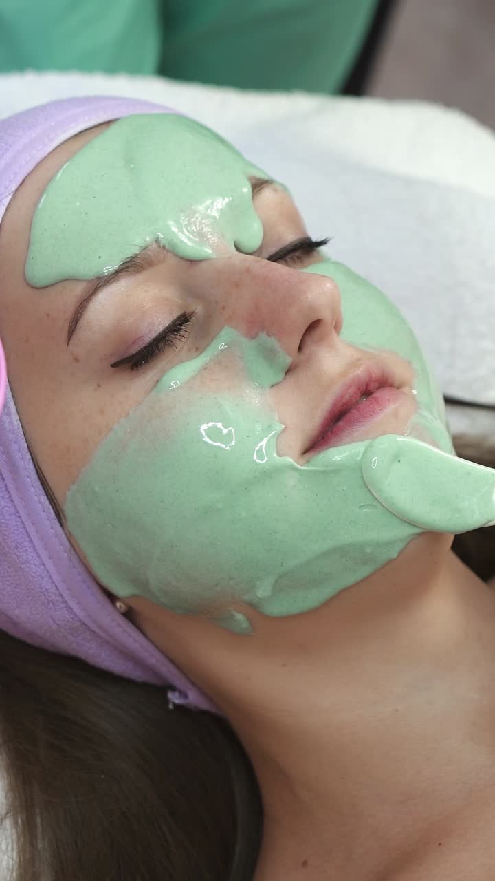 Mascarilla facial. Terapeuta aplicando mascarilla facial a una hermosa joven en un spa usando una brocha de cosméticos.