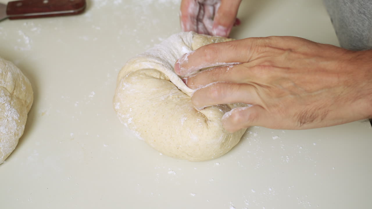 Top view of a Baker folding the dough and shaping it into a loaf of bread