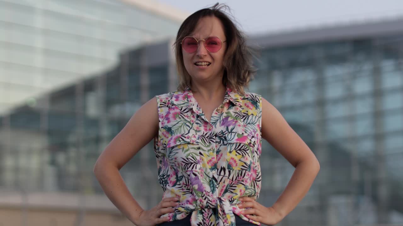 화가 난 미치광이 여성 관광객이 트렌디한 선글라스를 입고 주먹을 들어 격렬한 얼굴로 카메라를 쳐다보고 있습니다.