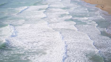 Picturesque-aerial-view-of-several-white-waves-of-blueish-green-ocean-rolling-towards-sandy-beach,-Gaeta,-Italy,-static