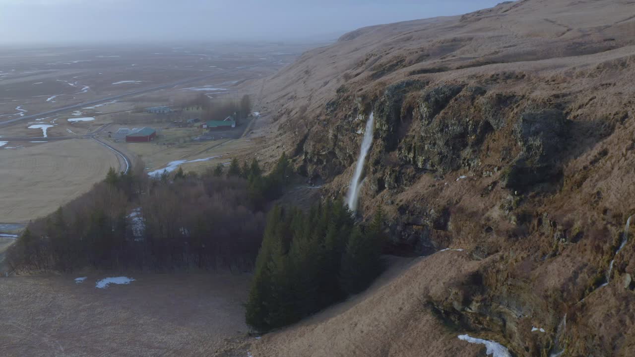 Letecký dronový záběr podél útesů s vodopády směrem k islandské farmě.