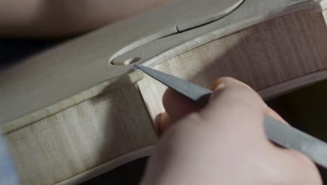 macro close up of artisan luthier maker work on new classic handmade raw violin smooth edge in waist and purfling rasp in workbench of workshop in cremona italy 4k video